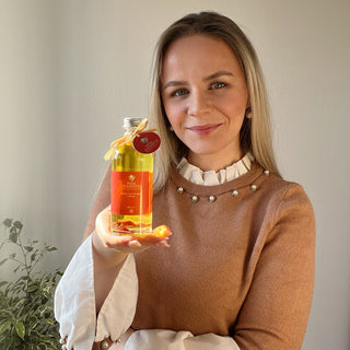 Strahlende Frau mit gesunder Haut hält das Pure Elements Körper- und Massageöl •Energie• in der rechten Hand. Sie lacht zufrieden – Sinnbild für natürliche Pflege bei trockener Haut. Hauptbild des Blogbeitrags „Was sind eure Geheimrezepte bei trockener Haut?“