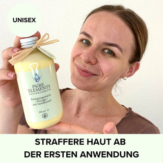 Frau hält die Reinigungsmilch •Energie• mit Sanddornöl von Pure Elements in der 200 ml Flasche. Sie strahlt Energie und Zufriedenheit aus. Das Bild betont die Unisex-Verwendung und den Effekt: Straffere Haut ab der ersten Anwendung. BDIH-zertifizierte Naturkosmetik, vegan, glutenfrei, mit echten Bergkristallen und tierversuchsfrei.